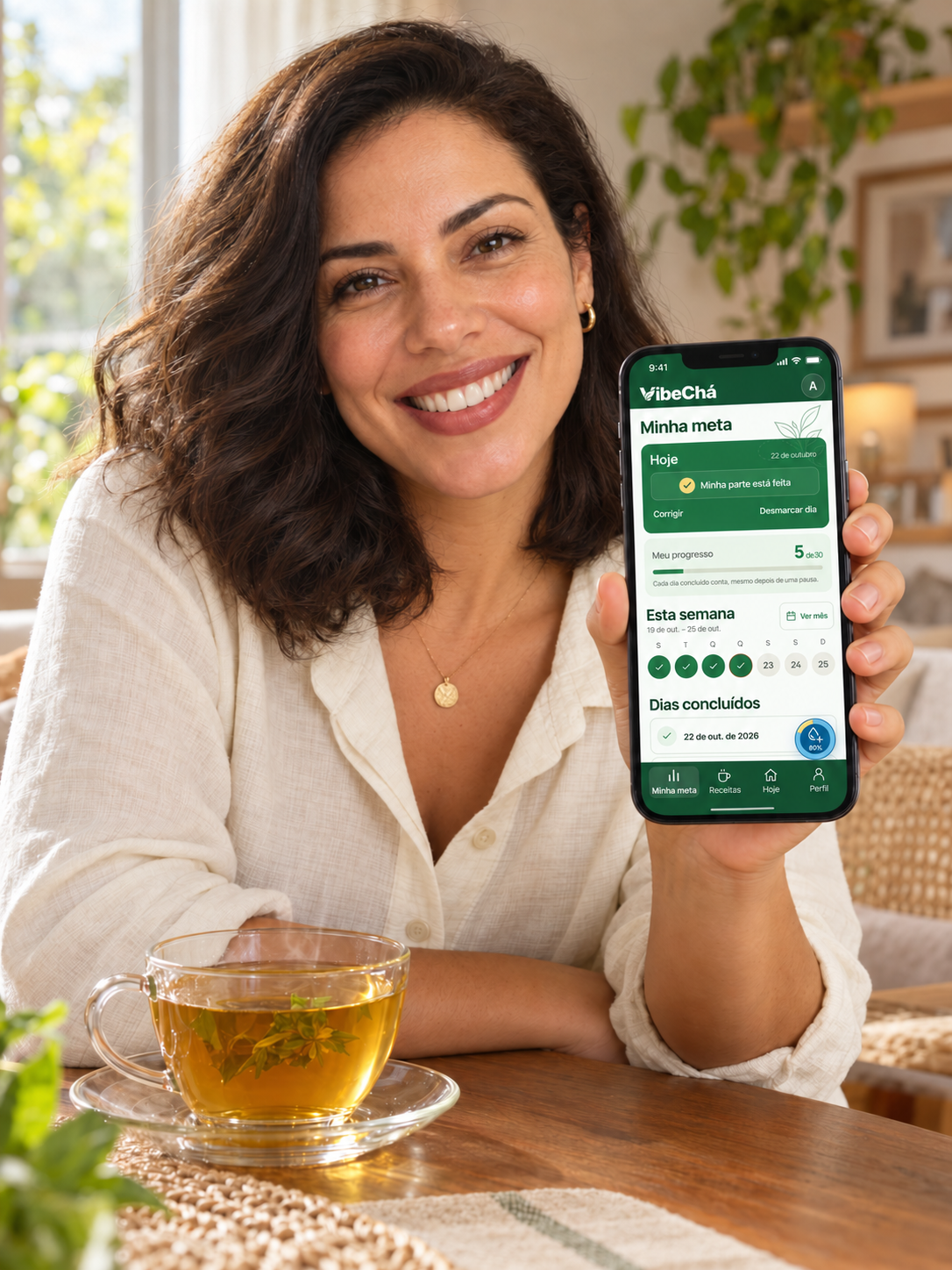 Mulher sorrindo com o aplicativo VibeChá no celular e uma xícara de chá na mesa